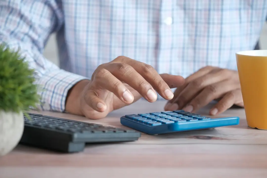 Hands use a calculator next to a keyboard on a desk to compare Nexus4kTV plan prices